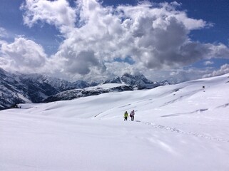 People walk in the distance in the mountains on a snow-covered slope. Two people in the snowy mountains climb up the hill