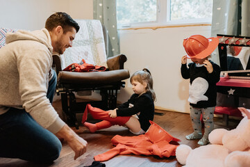 A father helping his two children getting dressed up as firefighters.