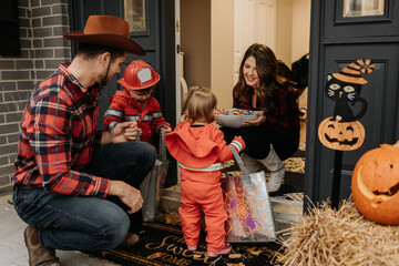 A family dressed up for Halloween trick or treating, collecting sweets from a woman at her door.