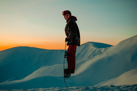 A man wearing a ski suit, helmet and goggles on a snowy mountain ridge at sunset