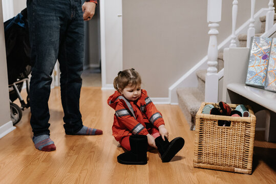 A little girl dressed as a firefighter sitting on a wooden floor pulling on black boots