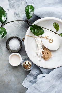 A marble bowl with a bar of soap, cotton buds and a necklace with bee motif next to bowls of cream and salt.