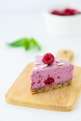 Slice of cold raw cashew cake with raspberries, mint and lime on a wooden board. Vegan dessert, sugar free, gluten, lactose.