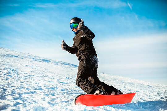 A person wearing a black ski suit, helmet and goggles skiing down a mountain on a red snowboard.