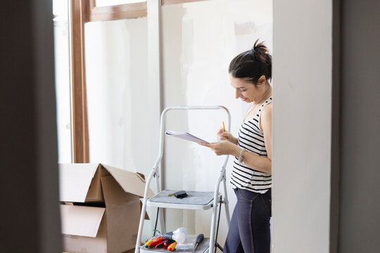 Woman looking at a pad of paper standing next to a stepladder and cardboard boxes.