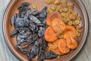 
dried fruits on a wooden plate raisins, prunes, apricot