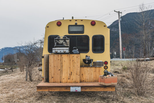 Rear view of a camper van with a wooden deck set up for a barbeque in a wintry rural landscape.