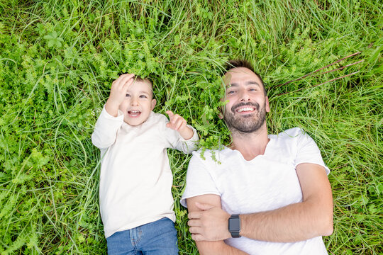 High angle view of smiling bearded man and young boy lying in grass.