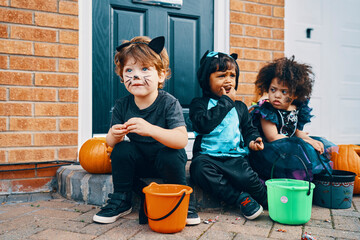 Three children dressed up for Halloween sitting on a doorstep eating sweets.