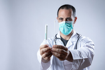 medico in camice bianco e stetofonendoscopio al collo indossa una mascherina chirurgica e mostra un...