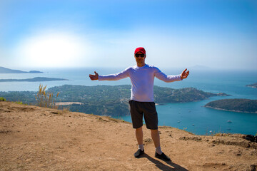 The young man shows his hand at the view from the mountain. Sportswear, cap. The Andamand Sea of Phuket Island, Thailand. Tropical exotic island.