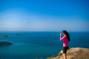 A young women brunette in pink dress watches, enjoys a view from the mountain. Sportswear, cap. The Andamand Sea of Phuket Island, Thailand.