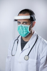 medico in camice bianco e stetofonendoscopio al collo indossa una mascherina chirurgica e una visiera protettiva in plexiglas   isolato su sfondo bianco