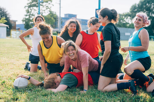 A group of women kneeling on a rugby pitch and laughing with one lying on the ground face down.