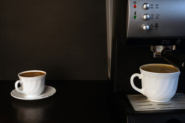 A coffee machine is standing on a black table. Two white cups with espresso. Place for text. Copyspace