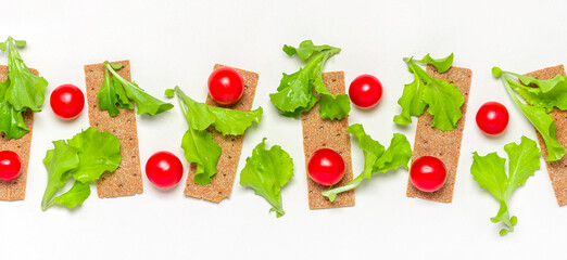 Crispbread, cherry tomatoes and fresh green lettuce leaves on a white background, top view, flat lay. Healthy food, fitness or diet concept. Ingredients for making sandwiches with crispbread. 