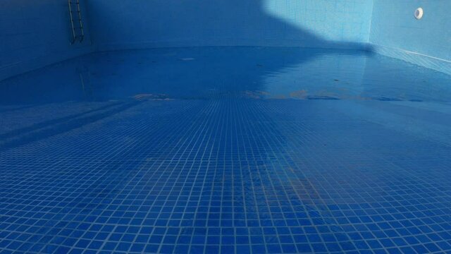 An empty swimming pool with blue tiles being filled with water at a constant rate.