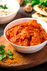 Chicken tikka masala in a white bowl, rice, spices and naan bread on a dark table, closeup. A traditional spicy Indian chicken dish. Chicken tikka.