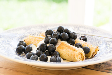 Morning breakfast with french crepes, fresh blueberry, yogurt on a plate on wooden table background. Side view.