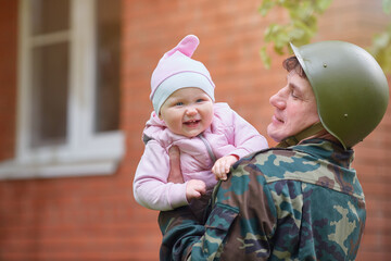 Military man in a helmet with a smiling little baby in his arms