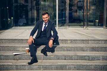 Happy brunette businessman sitting outside near office