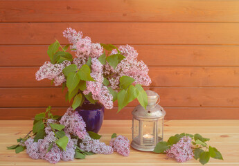 Branches of lilac in blue vase and lantern near on wooden table. Selective focus.