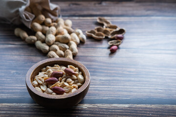 Peanuts in a wooden bowl on wooden table with peanuts in background.  Healthy snack. Close up view.