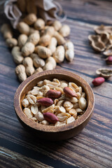 Peanuts in a wooden bowl on wooden background. Healthy snack. Vertical picture.