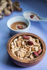 Natural peanuts in a wooden bowl with peanut butter in background. Healthy snack. Vertical picture.