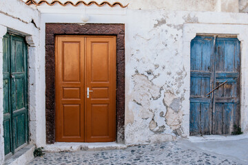 Fototapeta na wymiar Three old wooden doors in different colors. White stone wall. Traditional village of Pyrgos on Santorini island, Greece. 