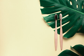 Bathroom essentials. Two wooden bamboo eco friendly toothbrushes and green leaves monstera on pastel beige background. Dental care and zero waste concept. Flat lay, top view, copy space
