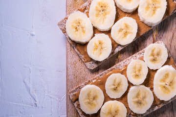 Swedish crispbread with almond butter and banana's slices on a wooden table on white background. Healthy snack. Top view.