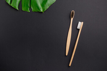 Flat lay composition with two wooden bamboo eco friendly toothbrushes, green leaves monstera and space for text on black background. Teeth hygiene. Top view, copy space