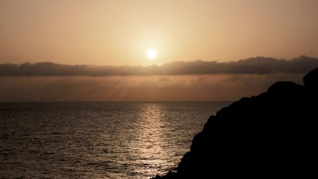 Sunset in the ocean in calm with lineal clouds in the horizont and a big rock and seagulls
