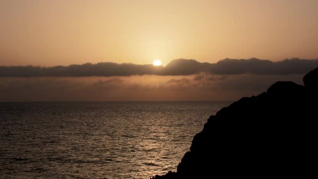 Sunset in the ocean in calm with lineal clouds in the horizont and a big rock