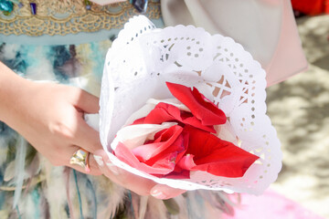 Pétalos de rosas rojas y rosadas en un cono de papel sostenido por la mano de una mujer.