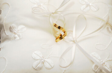 Par de anillos de oro sobre un pequeño cojín blanco.