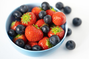 fresh strawberries and blueberries in a blue bowl on a white background close up