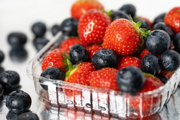 strawberries and blueberries in water drops in a transparent plastic container close up