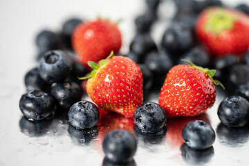 strawberries and blueberries in water drops on a reflective background close up