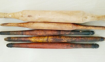 Set of wooden rolling pins with various colours, shapes and sizes on white floor, background.