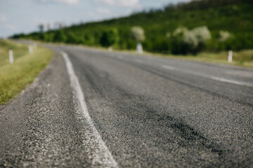 Damaged asphalt road in the countryside with tire marks. Closeup, shallow depth of field.