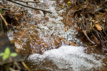 The water source flows down the rocks into the river. Water in the form of bubbles flows down the stones