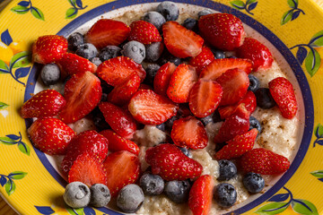 Oatmeal with fresh strawberries and frozen blueberries with cinnamon on a table in a plate