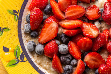 Oatmeal with fresh strawberries and frozen blueberries with cinnamon on a table in a plate