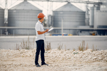 Engineer near the factory. Man in a helmet. Inspector looks at the building.