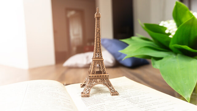 Bright room interior, sunlight. Open book, cup of tea. Eiffel tower figurine. Blue cup, soles. Bouquet of lilies of the valley with green leaves.