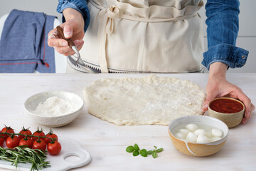 Woman adding tomato sauce on pizza. Woman doing homemade pizza.