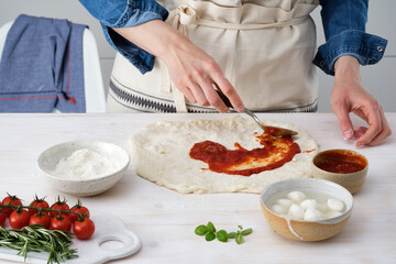 Woman adding tomato sauce on pizza. Woman doing homemade pizza.
