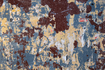 old gray beige wall with spots and stripes, scratches of brown and blue paint with scraps of paper ads. rough surface texture